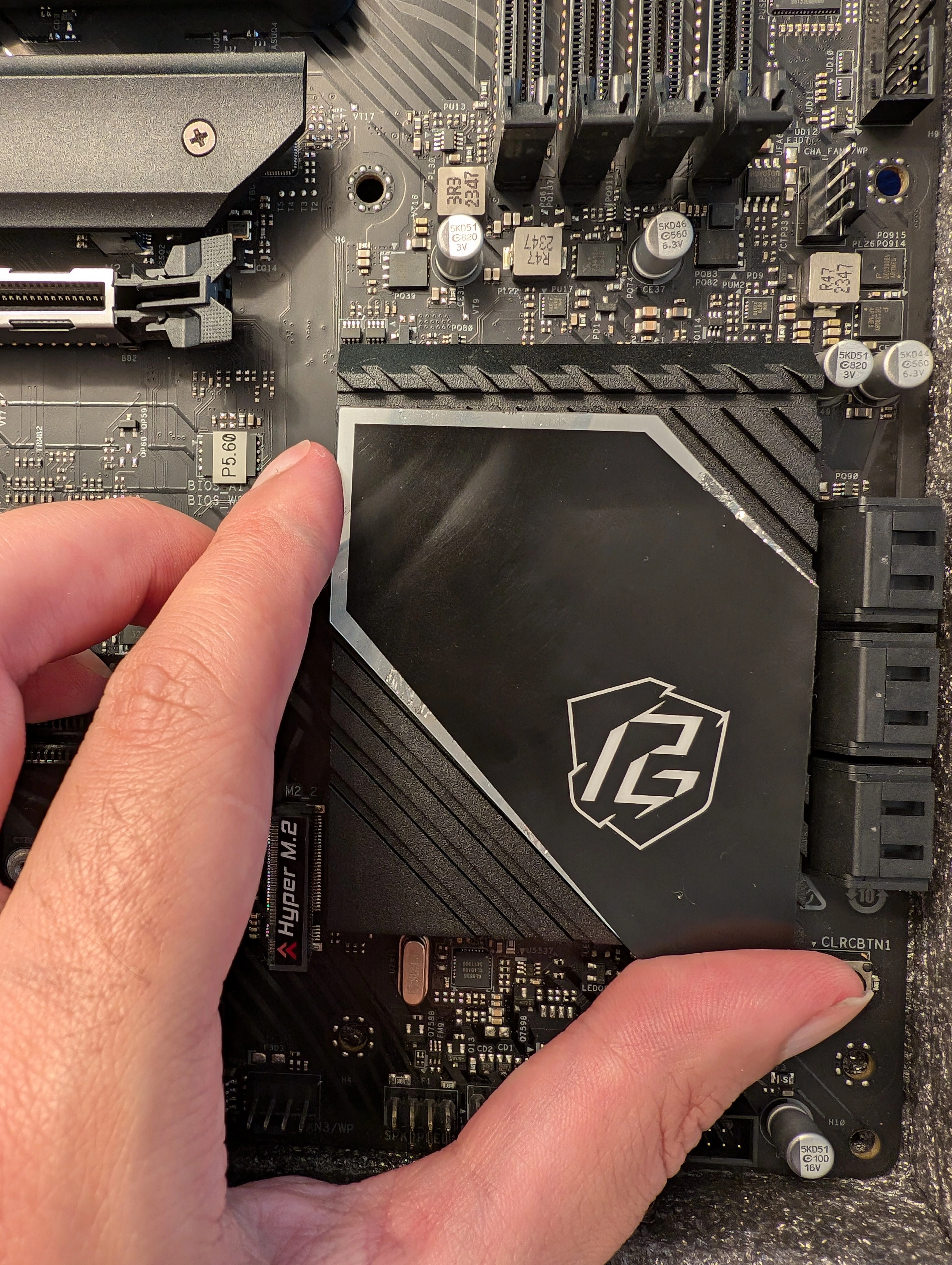 A hand removing the decorative sticker from the chipset heatsink of an ASRock motherboard