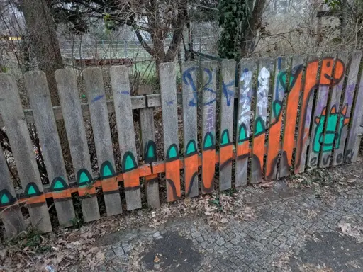 Orange dinosaur sprayed on wood fence, the dino has long neck and tail and green spikes on the back