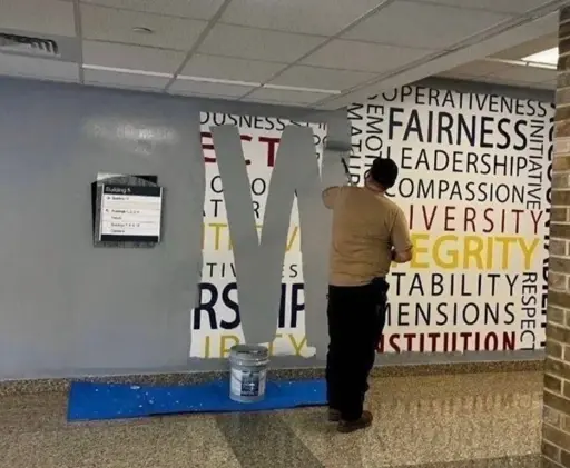 a man paints over a mural listing values such as fairness, leadership,  compassion, respect, stability,  and integrity