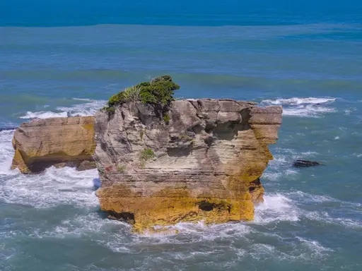 A rock outcropping in the middle of ocean waves.  The outcropping shows many thin layers, suggestive of a stack of pancakes layered one on top of the other